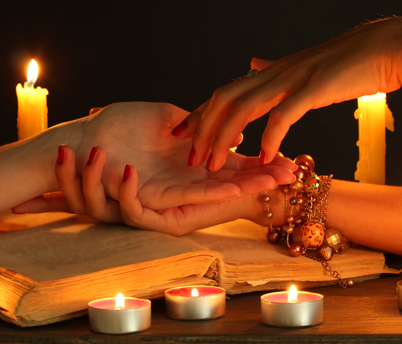 Palm reading being done by a psychic with candles burning on the table.